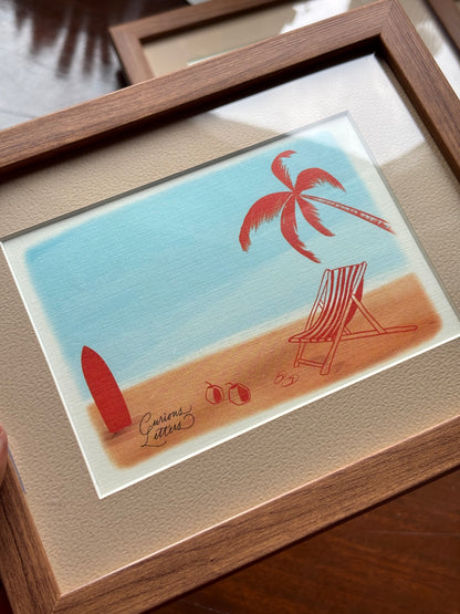 A framed art print depicting a beach scene with a red palm tree, red surfboard, striped beach chair, and red flip-flops on a sandy shore under a light blue sky, set in a brown wooden frame with a beige mat.